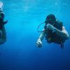 Dos buceadores disfrutan de las aguas cristalinas de la costa de Granada, uno de ellos ajustándose la máscara. Es una aventura perfecta con el "Paquete experiencia escapada de buceo en la costa de Granada". - ForTwo - Planes para parejas