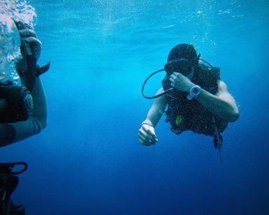 Dos buceadores disfrutan de las aguas cristalinas de la costa de Granada, uno de ellos ajustándose la máscara. Es una aventura perfecta con el "Paquete experiencia escapada de buceo en la costa de Granada". - ForTwo - Planes para parejas