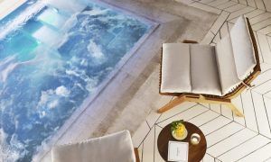 Un lujoso jacuzzi, dos sillas acolchadas y una pequeña mesa con un libro y una bebida sobre baldosas geométricas inspiradas en los elegantes años 20 crean el ambiente perfecto en Égoïste Spa. - ForTwo - Planes para parejas