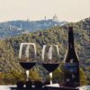 Dos copas de vino tinto y una botella sobre una mesa con las pintorescas colinas de Collserola al fondo, con un monumento a lo lejos. Perfecto para los amantes de la aventura. - ForTwo - Planes para parejas
