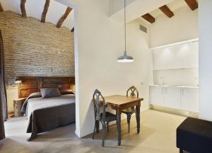 Encantador estudio con cama, pequeña mesa de comedor y cocina americana. Los detalles de ladrillo y madera aportan calidez. Ubicación ideal para disfrutar de aventuras enoturísticas con la Escapada de enoturismo de la mano del hotel Lotus Priorat en Falset (Tarragona). - ForTwo - Planes para parejas