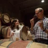 En una encantadora bodega cerca de Girona, dos invitados disfrutan de vino tinto en medio de grandes barriles de madera. Es un escenario ideal para un almuerzo íntimo y una visita a la bodega Mas Llunes (Garriguella, Girona). - ForTwo - Planes para parejas