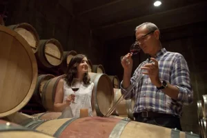 En una encantadora bodega cerca de Girona, dos invitados disfrutan de vino tinto en medio de grandes barriles de madera. Es un escenario ideal para un almuerzo íntimo y una visita a la bodega Mas Llunes (Garriguella, Girona). - ForTwo - Planes para parejas