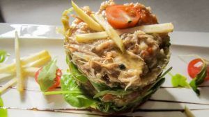 Una delicia culinaria: ensalada gourmet de atún con lechuga, tomates cherry y rodajas de manzana, rociada con salsa en un plato blanco, que evoca la elegancia del Restaurante Eustaquio Blanco (Cáceres). - ForTwo - Planes para parejas