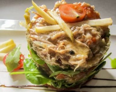 Una delicia culinaria: ensalada gourmet de atún con lechuga, tomates cherry y rodajas de manzana, rociada con salsa en un plato blanco, que evoca la elegancia del Restaurante Eustaquio Blanco (Cáceres). - ForTwo - Planes para parejas