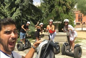 Cuatro personas en Segways, con cascos y sonrientes, posan en un parque con árboles y edificios mientras disfrutan de la pintoresca "Hacer una ruta en Segway por el Albaicín" a través del pintoresco paisaje. - ForTwo - Planes para parejas
