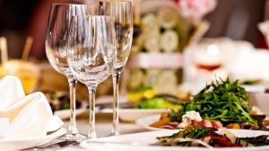 En el Hotel La Boroña, Escapada fin de semana (Gijón) incluye una mesa de comedor elegantemente puesta con copas de vino vacías y platos de ensalada, creando el ambiente perfecto para una escapada de fin de semana, realzado por decoraciones difusas que añaden un toque de misterio. - ForTwo - Planes para parejas