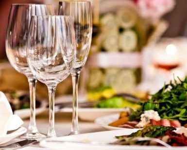 En el Hotel La Boroña, Escapada fin de semana (Gijón) incluye una mesa de comedor elegantemente puesta con copas de vino vacías y platos de ensalada, creando el ambiente perfecto para una escapada de fin de semana, realzado por decoraciones difusas que añaden un toque de misterio. - ForTwo - Planes para parejas
