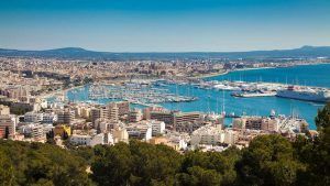 Una vista aérea de Palma de Mallorca revela una vibrante ciudad portuaria con barcos y edificios a lo largo de una resplandeciente costa azul. Cerca de allí, disfrute del lujo y relájese en el lujoso "Escapada con spa en el hotel HM Jaime III (Palma de Mallorca)" tras explorar los vibrantes alrededores. - ForTwo - Planes para parejas