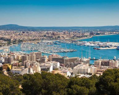 Una vista aérea de Palma de Mallorca revela una vibrante ciudad portuaria con barcos y edificios a lo largo de una resplandeciente costa azul. Cerca de allí, disfrute del lujo y relájese en el lujoso "Escapada con spa en el hotel HM Jaime III (Palma de Mallorca)" tras explorar los vibrantes alrededores. - ForTwo - Planes para parejas