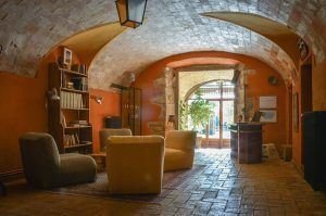 Una acogedora sala que evoca el encanto de una masía catalana del siglo XVIII, con techo abovedado, cómodos sillones y estanterías. La entrada, soleada y llena de plantas, da una cálida bienvenida, como la Escapada de quesos de Mas Alba. - ForTwo - Planes para parejas