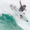 En Somo, un surfista del Curso de surf en la Escuela Cántabra de Surf desafía la gravedad sobre una ola turquesa con el cielo nublado como fondo. - ForTwo - Planes para parejas