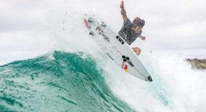 En Somo, un surfista del Curso de surf en la Escuela Cántabra de Surf desafía la gravedad sobre una ola turquesa con el cielo nublado como fondo. - ForTwo - Planes para parejas