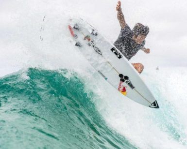 En Somo, un surfista del Curso de surf en la Escuela Cántabra de Surf desafía la gravedad sobre una ola turquesa con el cielo nublado como fondo. - ForTwo - Planes para parejas