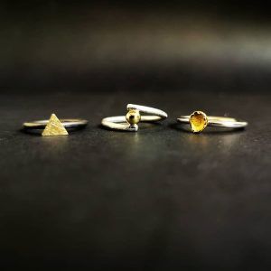 Tres anillos de plata con formas de triángulo, esfera y corazón se exhiben bellamente sobre una superficie oscura, ofreciendo una exquisita "Experiencia Joyero por un día" en el centro de Barcelona. - ForTwo - Planes para parejas