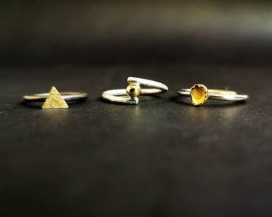 Tres anillos de plata con formas de triángulo, esfera y corazón se exhiben bellamente sobre una superficie oscura, ofreciendo una exquisita "Experiencia Joyero por un día" en el centro de Barcelona. - ForTwo - Planes para parejas