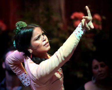 Una bailaora de flamenco cautiva al público borroso bajo las luces del escenario de Sevilla, que recuerdan a una "Escapada con bañera de hidromasaje, cava y crucero por el Guadalquivir", con el brazo levantado con pasión. - ForTwo - Planes para parejas