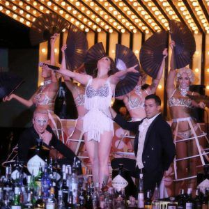 Artistas con trajes glamorosos cautivan el escenario en un espectáculo de la era Gatsby durante la Cena con espectáculo en Gatsby (Barcelona), mientras los fanáticos giran a su alrededor, reflejando la energía vibrante y las luces deslumbrantes de la ciudad. - ForTwo - Planes para parejas