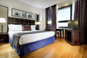 Experimente una comodidad inigualable en nuestra habitación bellamente decorada del Hotel Eurostars Gran Valencia, que cuenta con una cama doble con almohadas estampadas, pisos de madera, escritorio, TV y arte enmarcado en la pared. - ForTwo - Planes para parejas