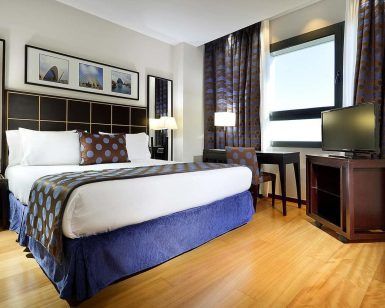 Experimente una comodidad inigualable en nuestra habitación bellamente decorada del Hotel Eurostars Gran Valencia, que cuenta con una cama doble con almohadas estampadas, pisos de madera, escritorio, TV y arte enmarcado en la pared. - ForTwo - Planes para parejas