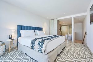 Disfrute de la elegancia moderna en el Hotel Eurostars Ibiza, donde le esperan una cama espaciosa, detalles azules, azulejos geométricos y un baño abierto con bañera y ducha. - ForTwo - Planes para parejas