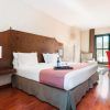 Descubra el encanto del Hotel Exe Agora en Cáceres, que ofrece una acogedora habitación con una cama amplia, detalles en rosa y suelo de madera. Relájese en el sillón rojo junto a la ventana, disfrutando de flores y vino servidos en una bandeja. - ForTwo - Planes para parejas