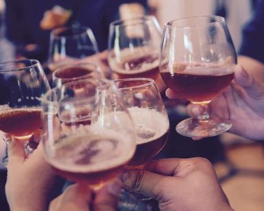 Primer plano de manos tintineando vasos de líquido ámbar durante un vibrante Taller de cata y degustación de cerveza en Barcelona. - ForTwo - Planes para parejas