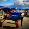 Un avión azul con ruedas rojas y una hélice se encuentra en la pista de Toledo bajo las nubes, listo para su próximo viaje como parte del "Curso de vuelo deportivo por un día (Toledo). - ForTwo - Planes para parejas