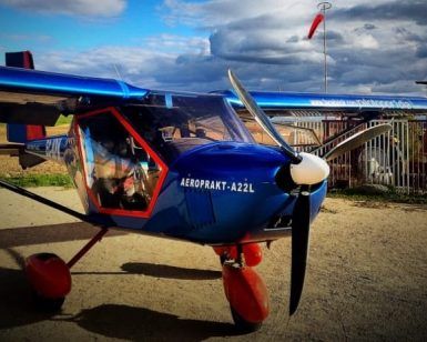 Un avión azul con ruedas rojas y una hélice se encuentra en la pista de Toledo bajo las nubes, listo para su próximo viaje como parte del "Curso de vuelo deportivo por un día (Toledo). - ForTwo - Planes para parejas