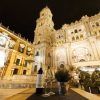 Una vista impresionante de la catedral de Málaga por la noche, complementada con una mesa bellamente puesta del Restaurante L'expérience (Málaga) con una botella de vino y copas, ideal para disfrutar de momentos bajo las estrellas. - ForTwo - Planes para parejas