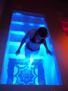 En una pequeña piscina con agua azul brillante, que evoca el ambiente relajante de una estancia en "Habitación doble y circuito de aguas saludables en Balneario de Lanjarón (Granada)", una persona se encuentra elegantemente en traje de baño. - ForTwo - Planes para parejas