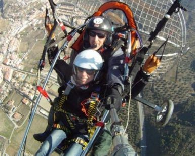 Con un palo de selfie en mano, dos aventureros disfrutan de un emocionante vuelo en paramotor en Granada, capturando impresionantes vistas del paisaje y la ciudad. Volar en parapente sobre Granada crea recuerdos inolvidables con su impresionante telón de fondo. - ForTwo - Planes para parejas