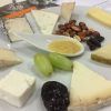 Disfruta del "Taller de cata y degustación de quesos artesanos en Barcelona", con una selección de quesos artesanales con frutos secos, miel, uvas y frutos secos en un plato blanco, perfecto para una experiencia de degustación de quesos. - ForTwo - Planes para parejas