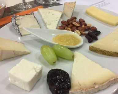 Disfruta del "Taller de cata y degustación de quesos artesanos en Barcelona", con una selección de quesos artesanales con frutos secos, miel, uvas y frutos secos en un plato blanco, perfecto para una experiencia de degustación de quesos. - ForTwo - Planes para parejas
