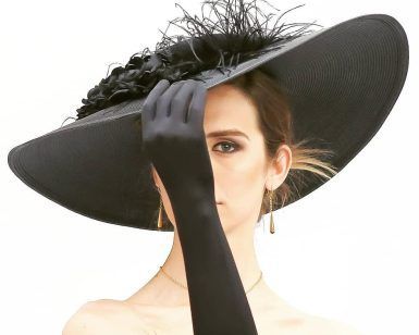 Una mujer con sombrero negro y guantes se cubre la mitad de la cara con la mano contra un fondo de estudio blanco, exudando elegancia y misterio que recuerda a una clásica "Sesión de fotografía de pareja de estudio (Madrid)", combinando el encanto sin esfuerzo. - ForTwo - Planes para parejas