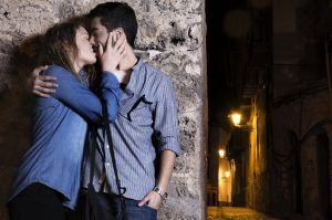 En la encantadora Granada, una pareja se besa contra un muro de piedra en una calle con poca luz por la noche, capturando el romance de "Un paseo de fotografía en pareja en Granada. - ForTwo - Planes para parejas