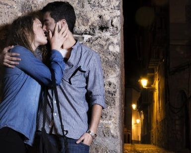 En la encantadora Granada, una pareja se besa contra un muro de piedra en una calle con poca luz por la noche, capturando el romance de "Un paseo de fotografía en pareja en Granada. - ForTwo - Planes para parejas