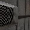 Un pasillo poco iluminado con una rejilla de ventilación metálica sobre una pared texturizada evoca la emoción de Prison Break de Fox in a Box Escape Room (Badajoz), proyectando sombras intrigantes en la superficie. - ForTwo - Planes para parejas