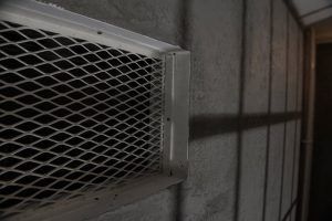 Un pasillo poco iluminado con una rejilla de ventilación metálica sobre una pared texturizada evoca la emoción de Prison Break de Fox in a Box Escape Room (Badajoz), proyectando sombras intrigantes en la superficie. - ForTwo - Planes para parejas