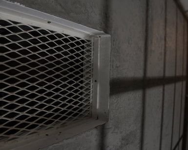 Un pasillo poco iluminado con una rejilla de ventilación metálica sobre una pared texturizada evoca la emoción de Prison Break de Fox in a Box Escape Room (Badajoz), proyectando sombras intrigantes en la superficie. - ForTwo - Planes para parejas