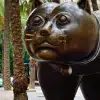En El Raval, una gran escultura de bronce de un gato cautiva a los visitantes entre palmeras y edificios animados. Descubra esta icónica imagen en el "Tour gratuito por el barrio del Raval (Barcelona)" mientras explora las vibrantes calles de Barcelona. - ForTwo - Planes para parejas
