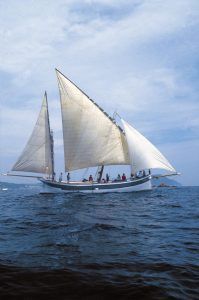 La Garoinada a bordo de un velero de época en Palamós ofrece una pintoresca escena de grandes velas deslizándose en el océano bajo un cielo azul con nubes, capturando el encanto marítimo de la fiesta tradicional. - ForTwo - Planes para parejas