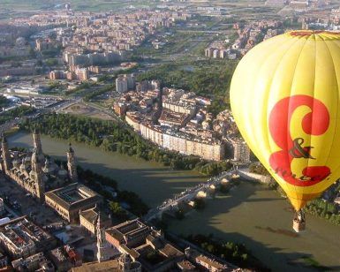 Un globo Vuelo en Globo por Globosreal (Zaragoza) en vibrantes tonos amarillos y rojos se eleva con gracia sobre Zaragoza, resaltando sus edificios históricos y su serpenteante río. - ForTwo - Planes para parejas