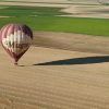 Un globo aerostático con Muga a bordo se desplaza suavemente sobre un vasto campo en La Rioja, proyectando una larga sombra que recuerda a la aventura Vuelo en globo por La Rioja con Globos Arcoiris. - ForTwo - Planes para parejas