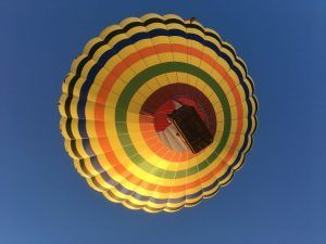 Experimente "Vuelo en globo con noche en hotel 4 estrellas (Antequera)": vea un globo aerostático con rayas de colores volando contra el cielo azul claro, perfecto para su estadía en un hotel de 4 estrellas en Antequera. - ForTwo - Planes para parejas