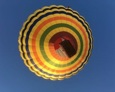 Experimente "Vuelo en globo con noche en hotel 4 estrellas (Antequera)": vea un globo aerostático con rayas de colores volando contra el cielo azul claro, perfecto para su estadía en un hotel de 4 estrellas en Antequera. - ForTwo - Planes para parejas