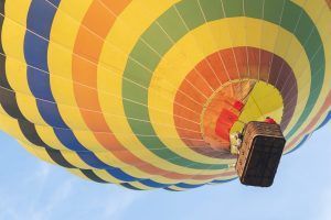 El Vuelo en Globo con Globotur en Sevilla ofrece una experiencia inolvidable mientras un vibrante globo aerostático con una cesta asciende con gracia contra el cielo azul claro. - ForTwo - Planes para parejas