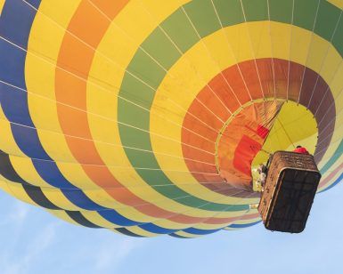 El Vuelo en Globo con Globotur en Sevilla ofrece una experiencia inolvidable mientras un vibrante globo aerostático con una cesta asciende con gracia contra el cielo azul claro. - ForTwo - Planes para parejas
