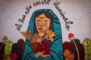 Explora un inspirador mural alternativo en Bilbao con un tour gratuito alternativo. Representa a una mujer vestida de azul con un corazón entre plantas vibrantes y presenta el conmovedor mensaje "al que esté triste ilumínalo", que le dará profundidad e iluminación a tu día. - ForTwo - Planes para parejas