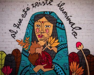 Explora un inspirador mural alternativo en Bilbao con un tour gratuito alternativo. Representa a una mujer vestida de azul con un corazón entre plantas vibrantes y presenta el conmovedor mensaje "al que esté triste ilumínalo", que le dará profundidad e iluminación a tu día. - ForTwo - Planes para parejas